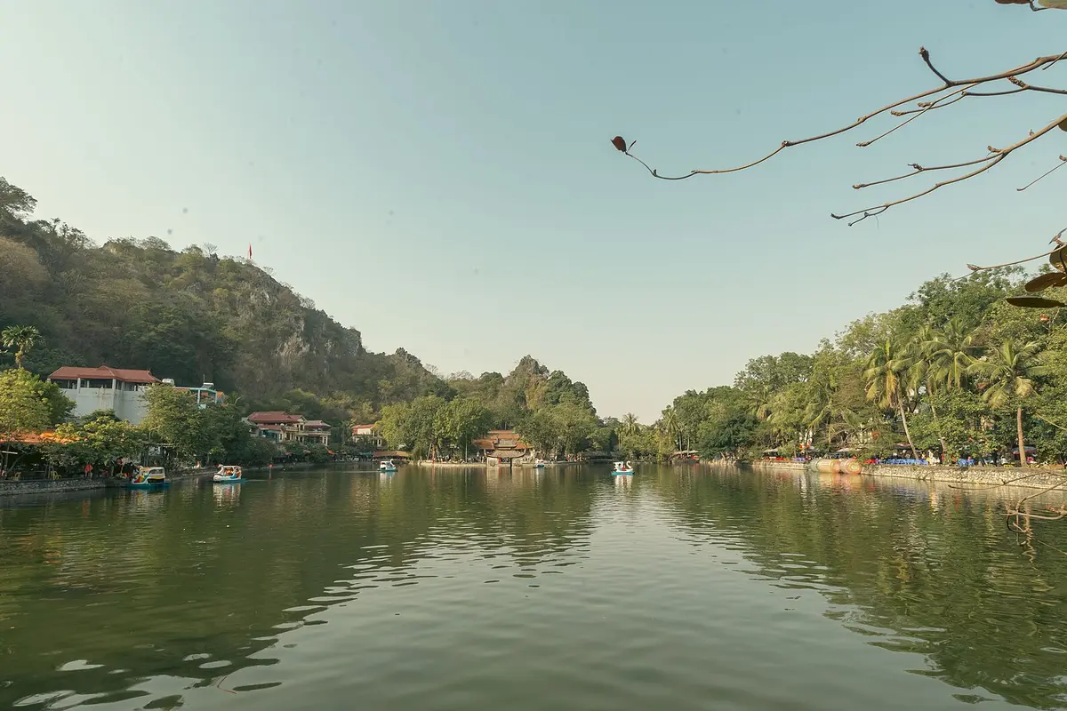 A wide green lake below a steep wooded limestone hill, with small boats on the water and a pavilion in the distance
